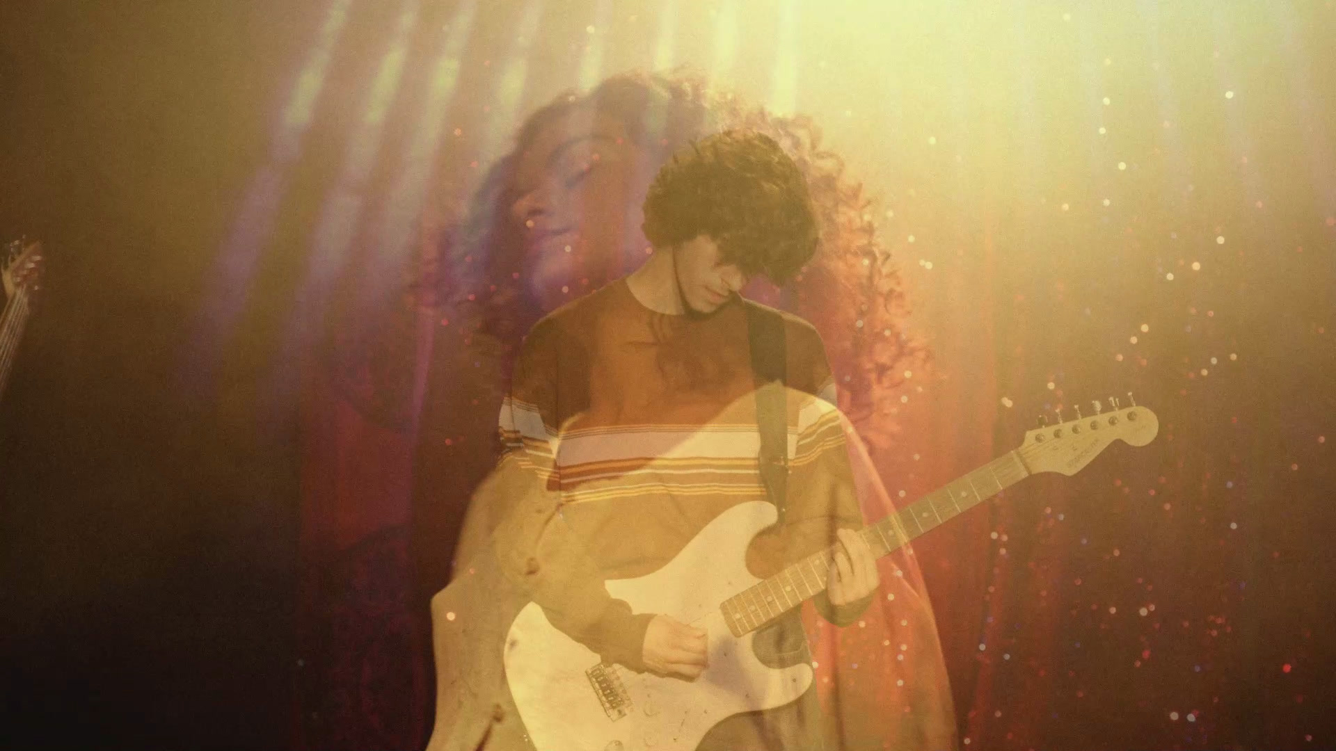 A guitarist layered with a woman's portrait in golden stage light